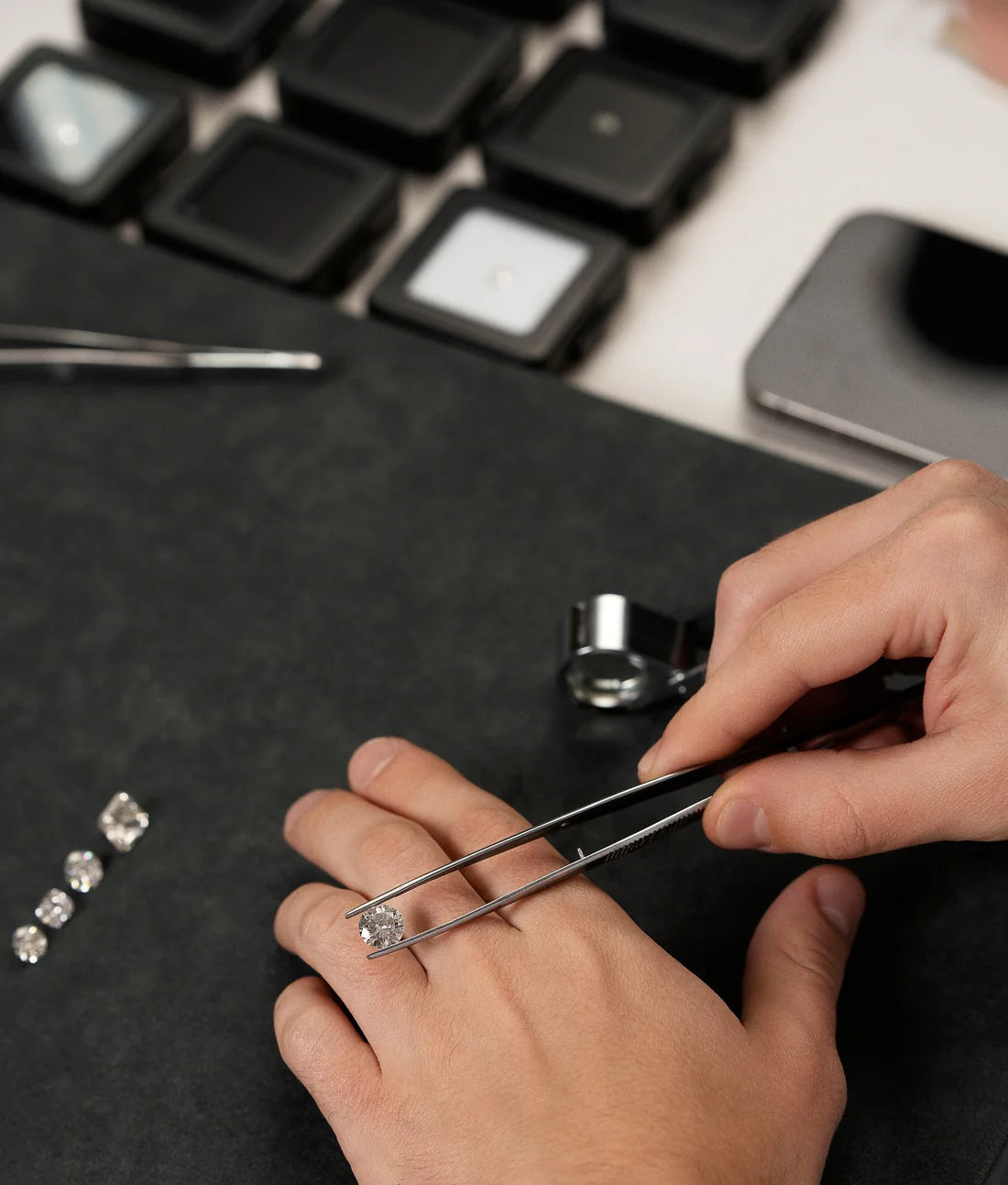 Person using tweezers to handle small diamonds on a dark surface with a keyboard in the background
